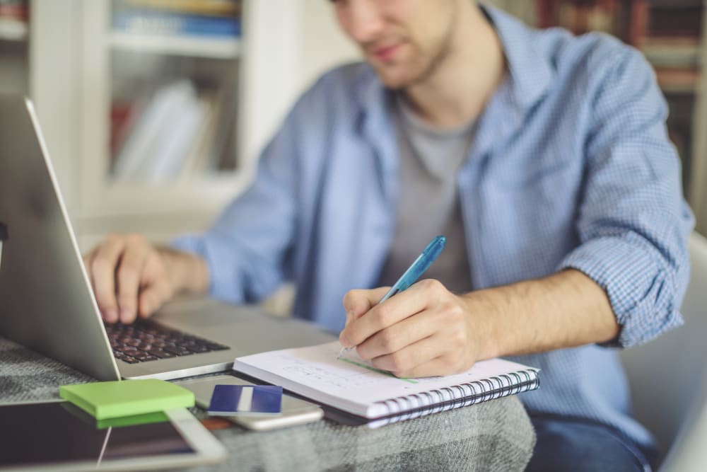 Image of person working at their desk with a laptop and pen and paper